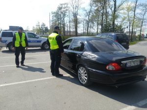 Policjanci kontrolują samochód koloru czarnego. Podają przyczynę kontroli oraz proszą o okazanie wymaganych dokumentów.