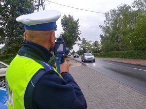 Policjant ruchu drogowego przy użyciu laserowego miernika prędkości wykonuje pomiar prędkości nadjeżdżających w jego kierunku pojazdów.