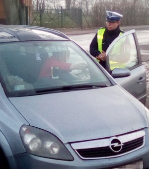Policjant ruchu drogowego podczas rozmowy z kierowcą samochodu osobowego. Funkcjonariusz stoi obok pojazdu, natomiast kierowca siedzi za kierownicą.