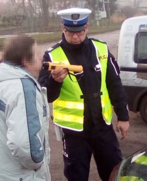 Policjant ruchu drogowego sprawdza alkomatem stan trzeźwości kierującego.