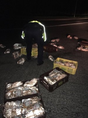 Policjant ubrany w żółtą kamizelkę odblaskową zbiera bochenki chleba z drogi.