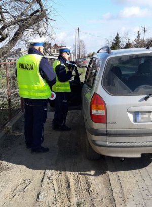 Policjanci żnińskiej drogówki podczas kontroli drogowej. Z prawej strony kontrolowany pojazd marki Opel. Z lewej stojący na poboczu policjanci. Jeden z funkcjonariuszy okazuje kierowcy zarejestrowany pomiar prędkości.
