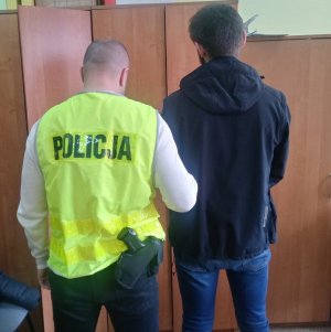 Z lewej strony policjant w żółtej kamizelce odblaskowej, z prawej zatrzymany mężczyzna do sprawy przywłaszczenia telefonu.
