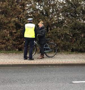 Policjant podczas kontroli rowerzysty. Obydwoje stoją na chodniku położonym blisko ulicy.